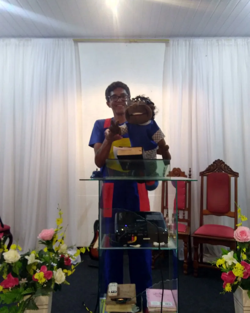 Beto e um fantoche atrás de um púlpito de vidro, em uma igreja