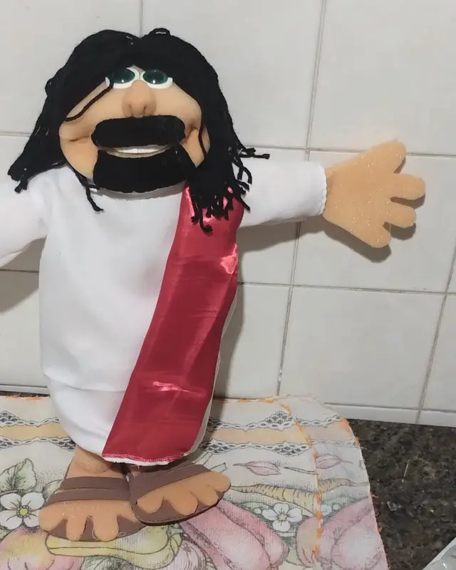 Jesus, fantoche de cabelo e barba pretos, túnica branca e faixa vinho