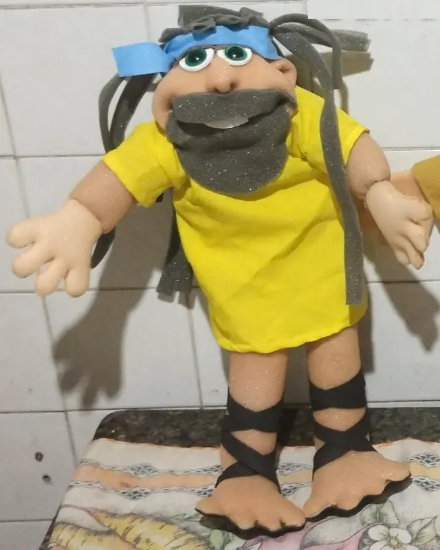 Sansão, fantoche de barba cinza, faixa azul na cabeça e túnica amarela