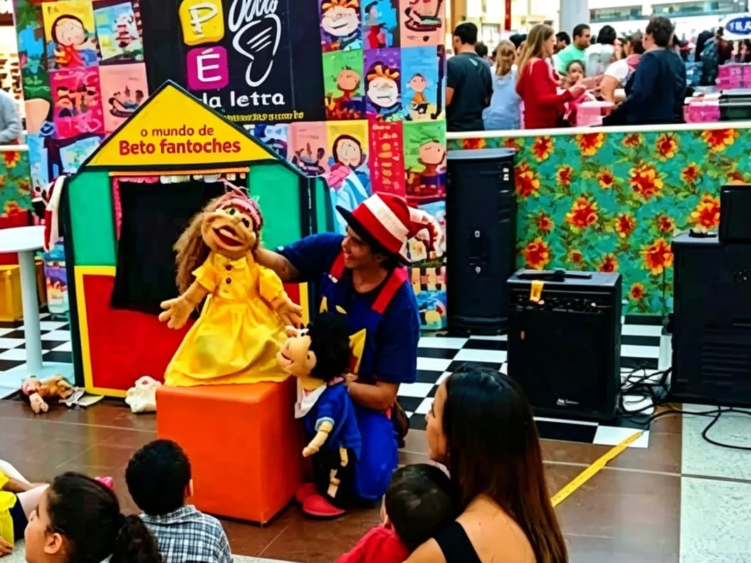 Beto contando uma história com fantoches para crianças sentadas no chão de um shopping